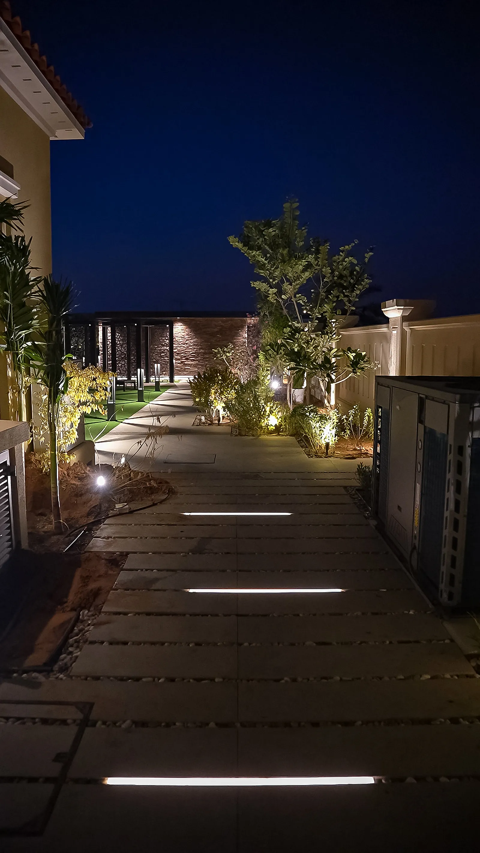 Linear fittings recessed flush between paving sections along the garden path, with uplit planting either side