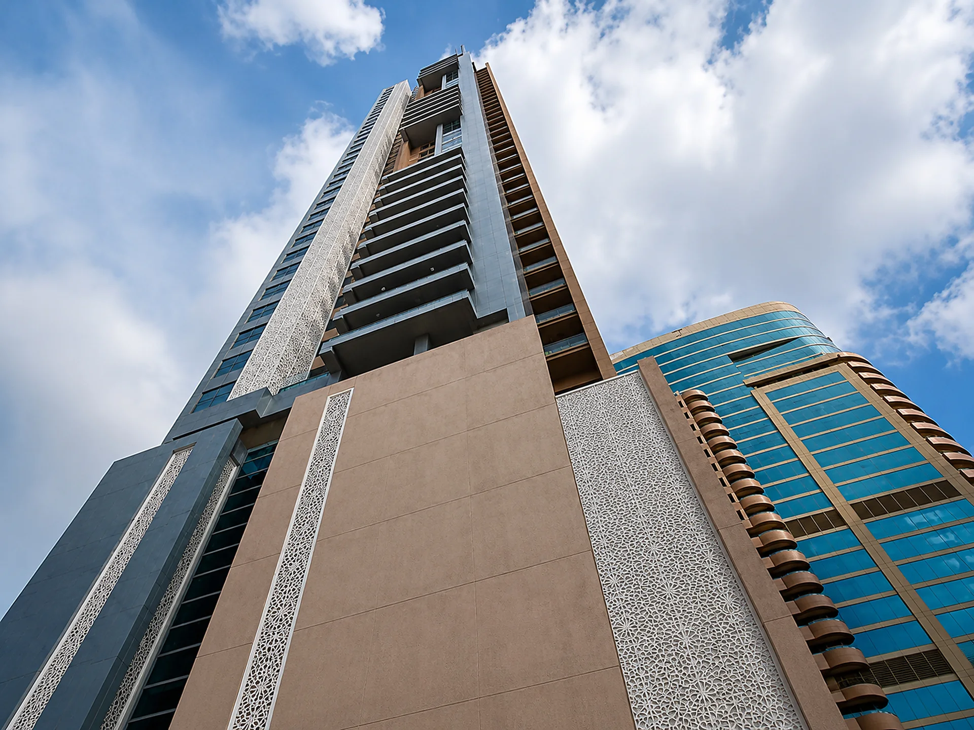 The built elevation of Al Qasimia University Endowment Tower seen from street level in daylight, with narrow perforated geometric screens set into the podium wall