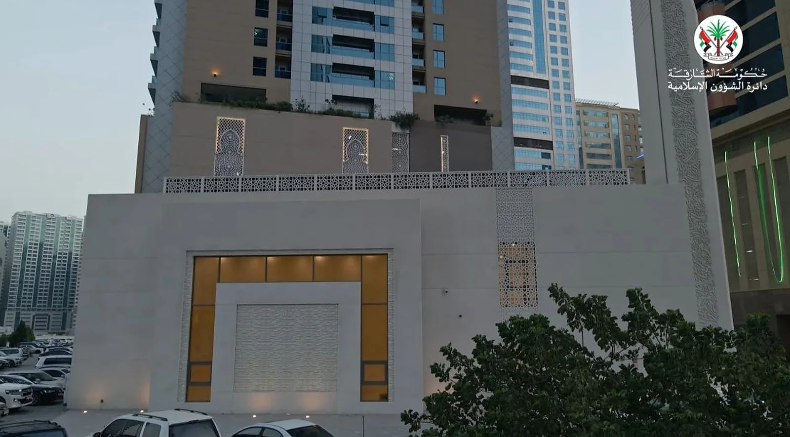 Al Rajaa Mosque in Sharjah at dusk, its perforated parapet screens and lit entrance portal