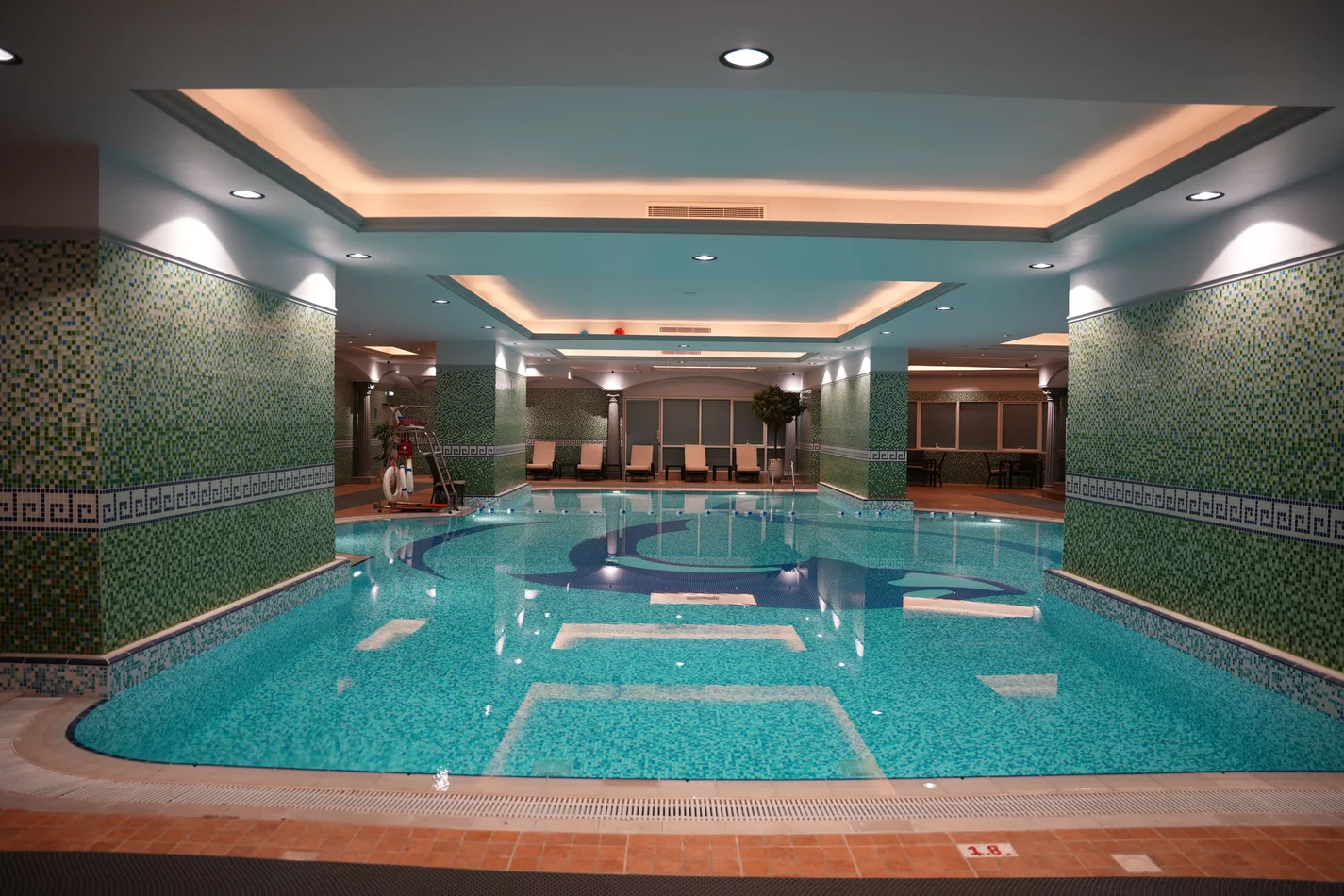 The indoor swimming pool at Al-Serh Gym, lit from a perimeter cove around the ceiling recess and by downlights close to the tiled walls