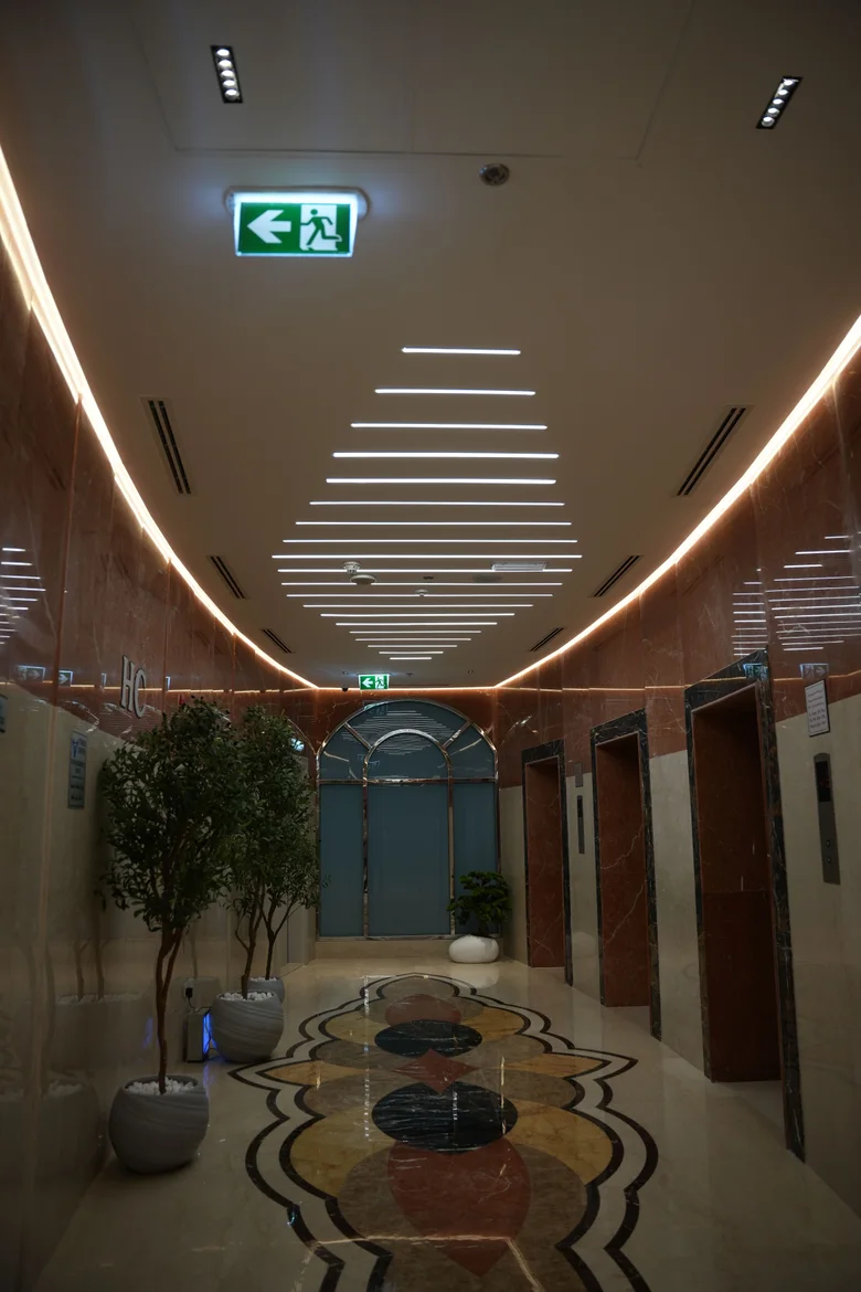 The lift lobby at Al-Serh Gym, with a warm cove following the curved ceiling edge and stepped linear bars running the length of the corridor