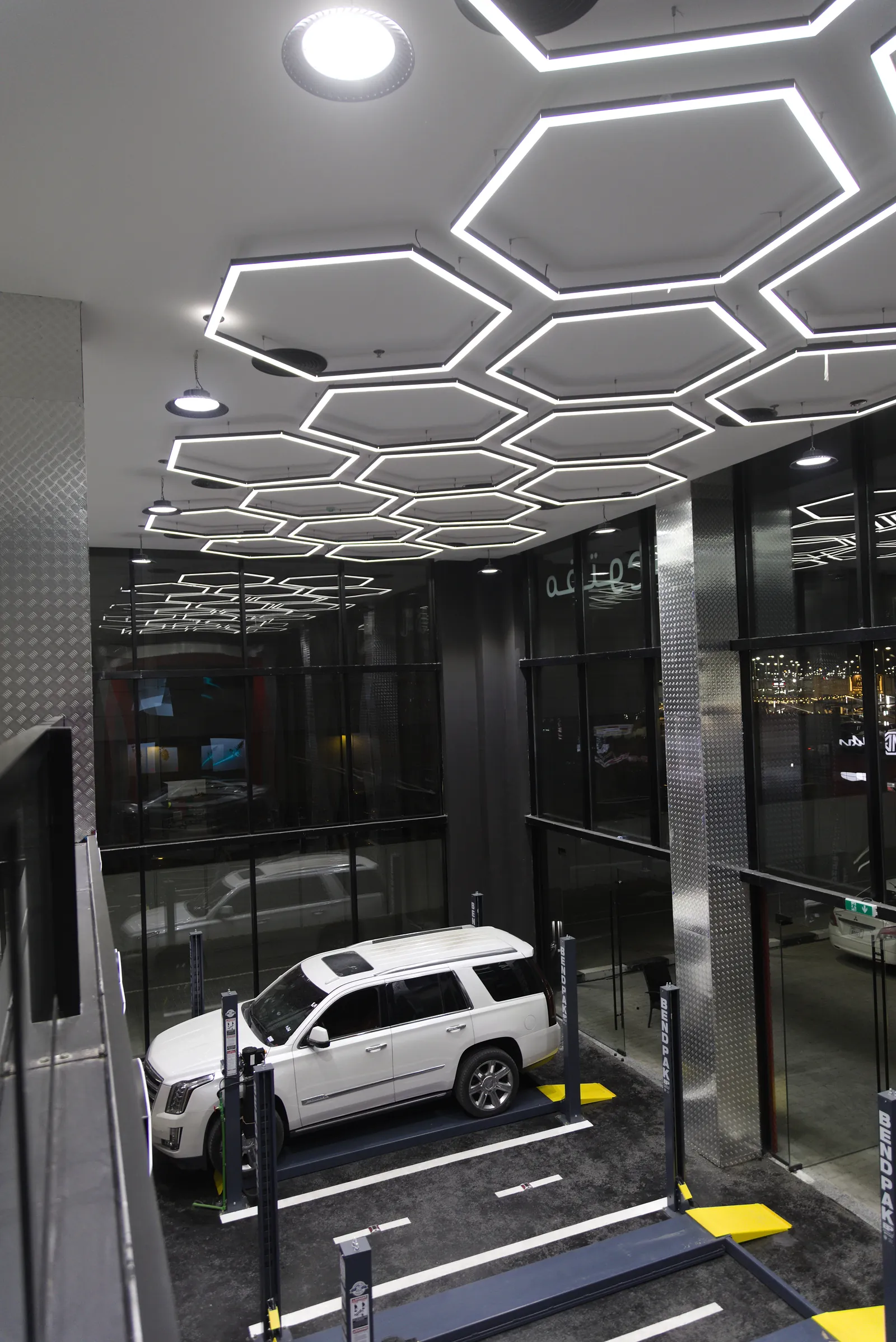 The vehicle testing bays at Al Weam and Al Aman, lit by a continuous hexagonal grid of linear fittings above four-post lifts