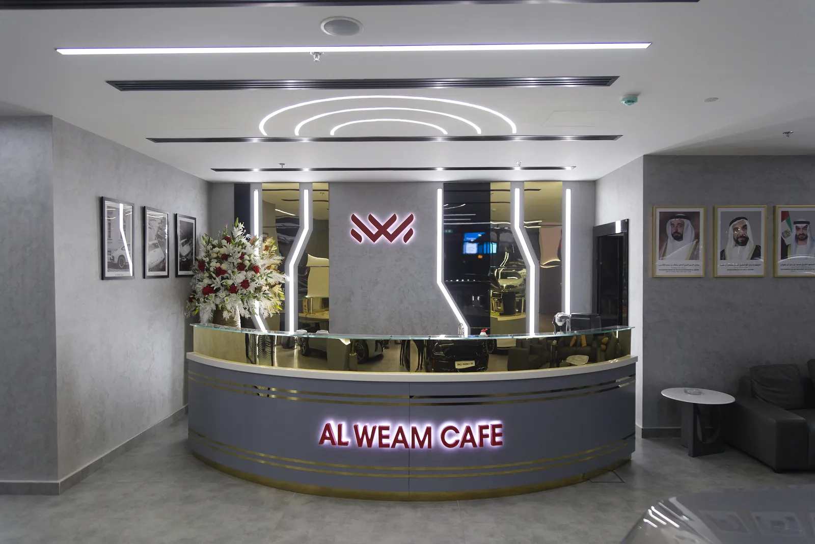 The reception and cafe counter at Al Weam, with concentric lit arcs in the ceiling and a backlit brand mark on the wall behind