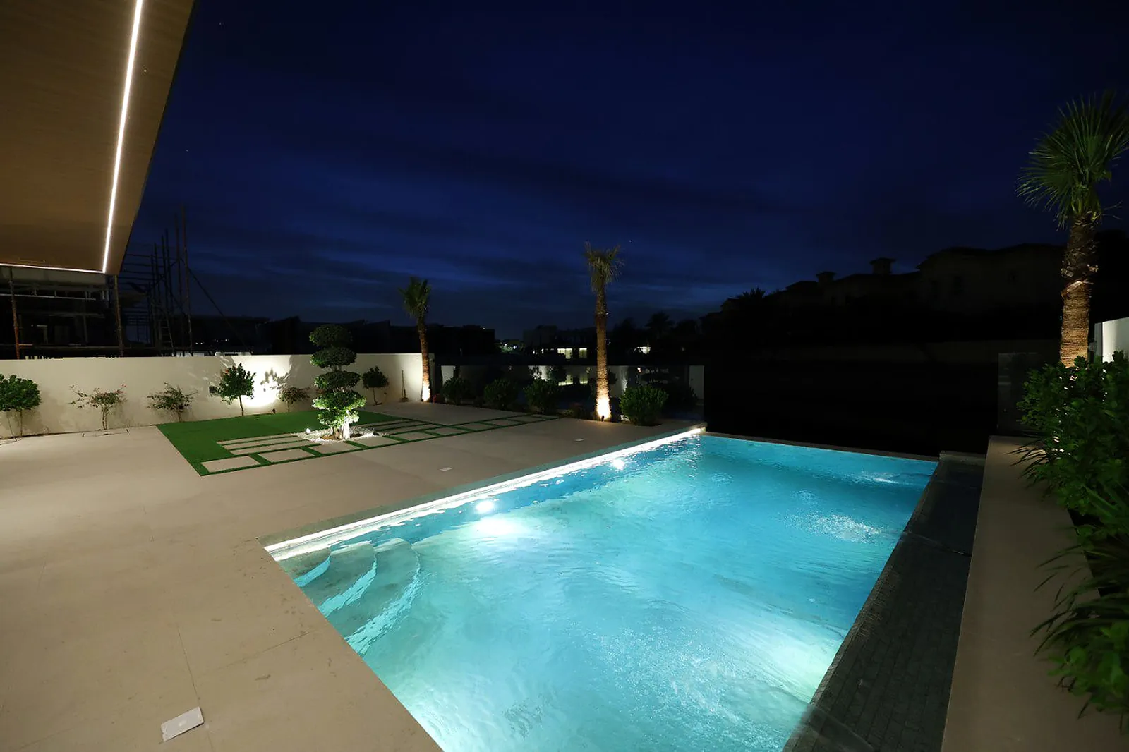 A linear run in the pool coping and uplit palms beyond, at the Alkhafaji villa in Dubai