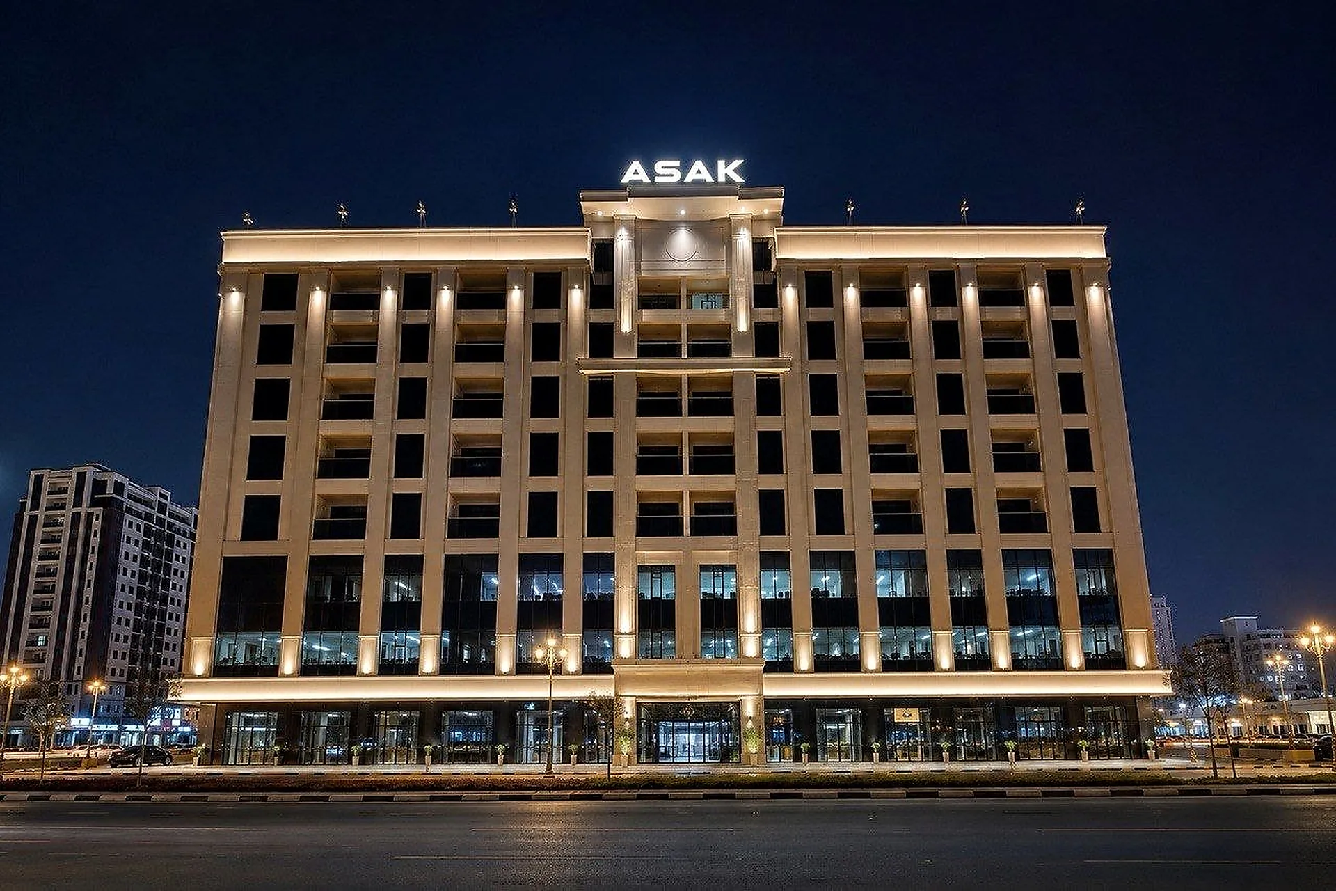 The symmetrical elevation of the Asak Building in Sharjah at night, its vertical piers lit individually and a continuous run along the roof cornice
