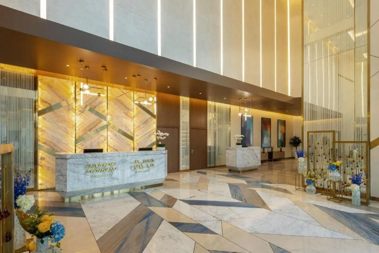 The double-height main lobby at Aykon City, with a backlit stone reception desk, gold vertical fins and a patterned marble floor