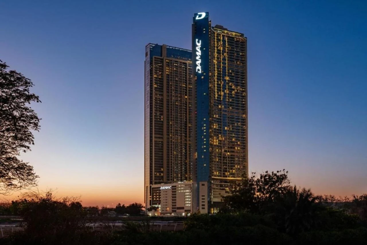 Aykon City Tower Block B and C at dusk, seen from a distance with the DAMAC signage lit