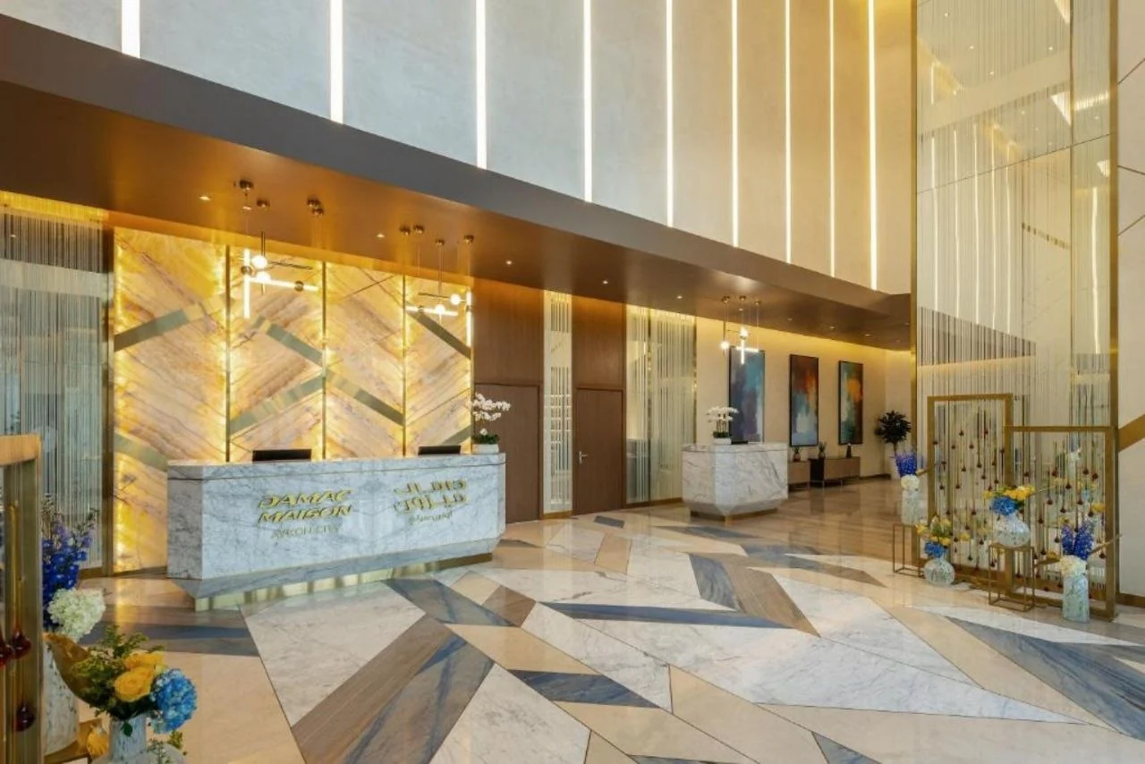 The double-height hotel lobby at Aykon City, with a backlit stone reception wall and vertical slots in the ceiling coffer