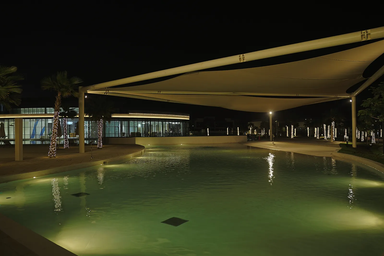 A tensile fabric canopy over the pool at Dubai South, lit from below so the underside of the fabric becomes the light source