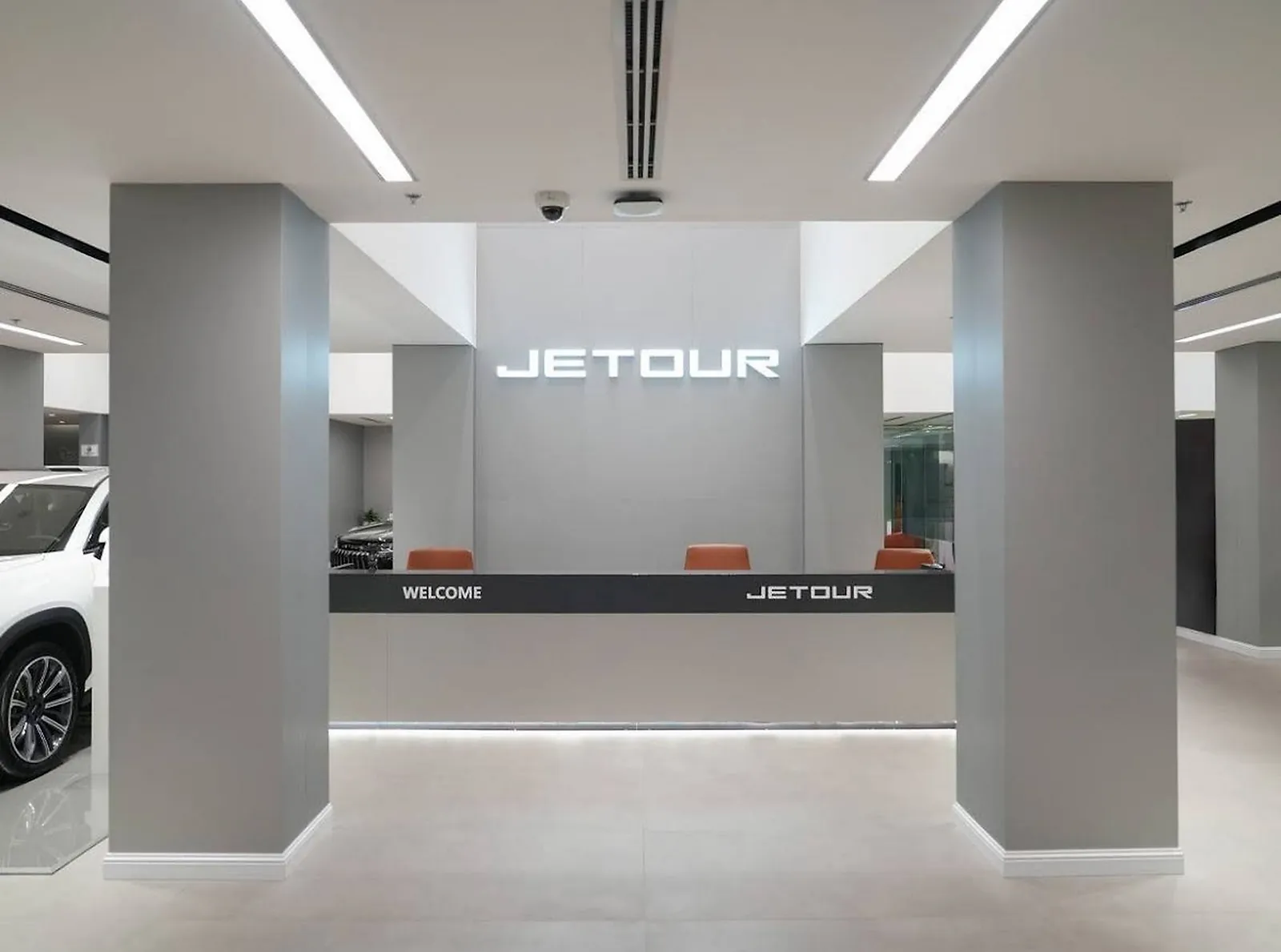 The reception desk at the Jetour showroom, with a backlit brand sign and recessed linear runs in the ceiling