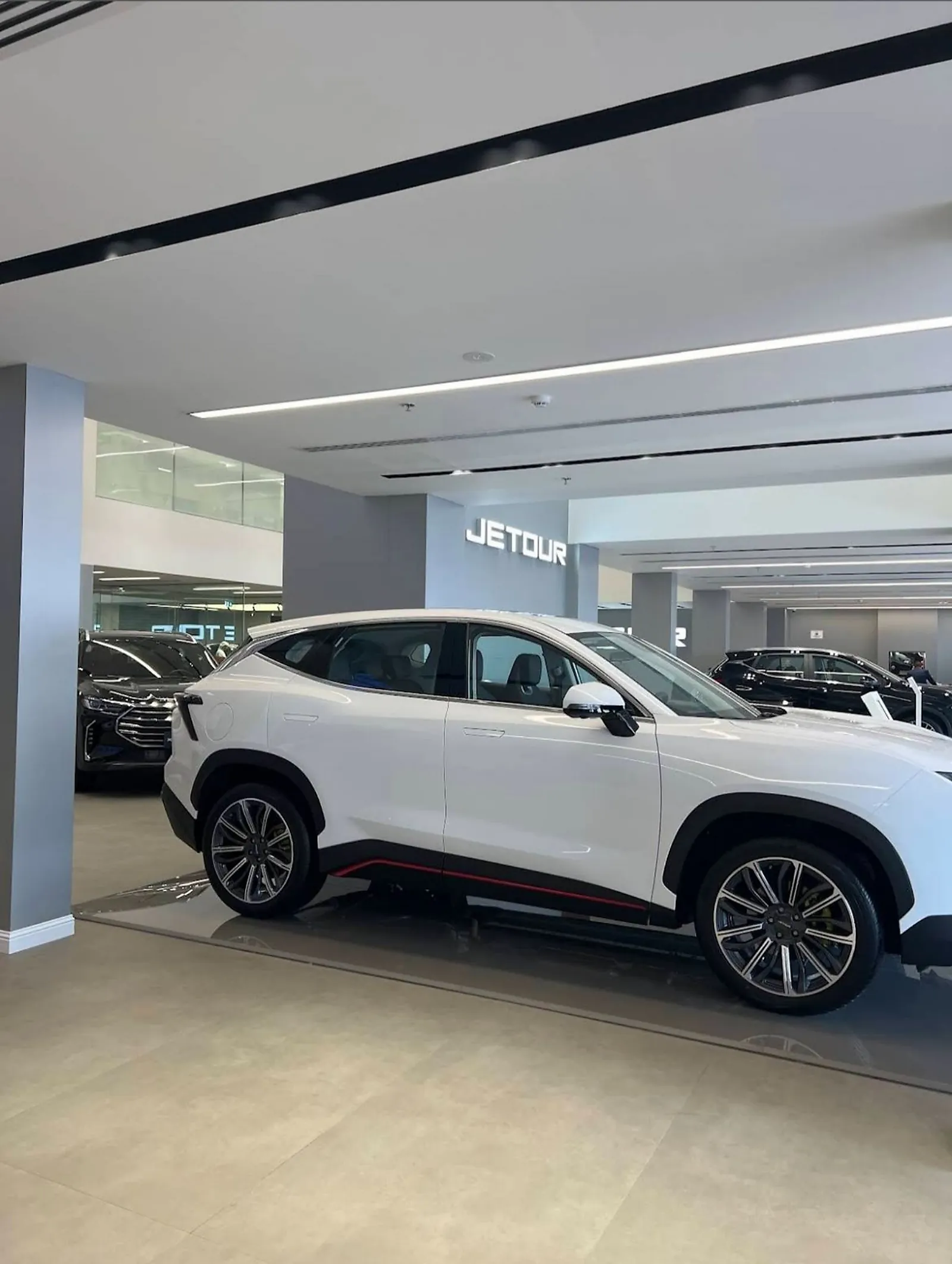 A white SUV on the display floor at the Jetour showroom, lit from recessed linear runs overhead