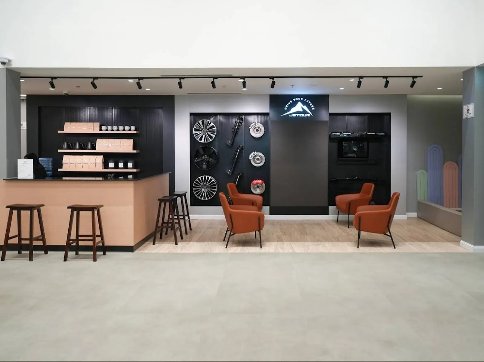 The customer lounge and accessory wall at the Jetour showroom, with track spots on the display and a coffee counter alongside