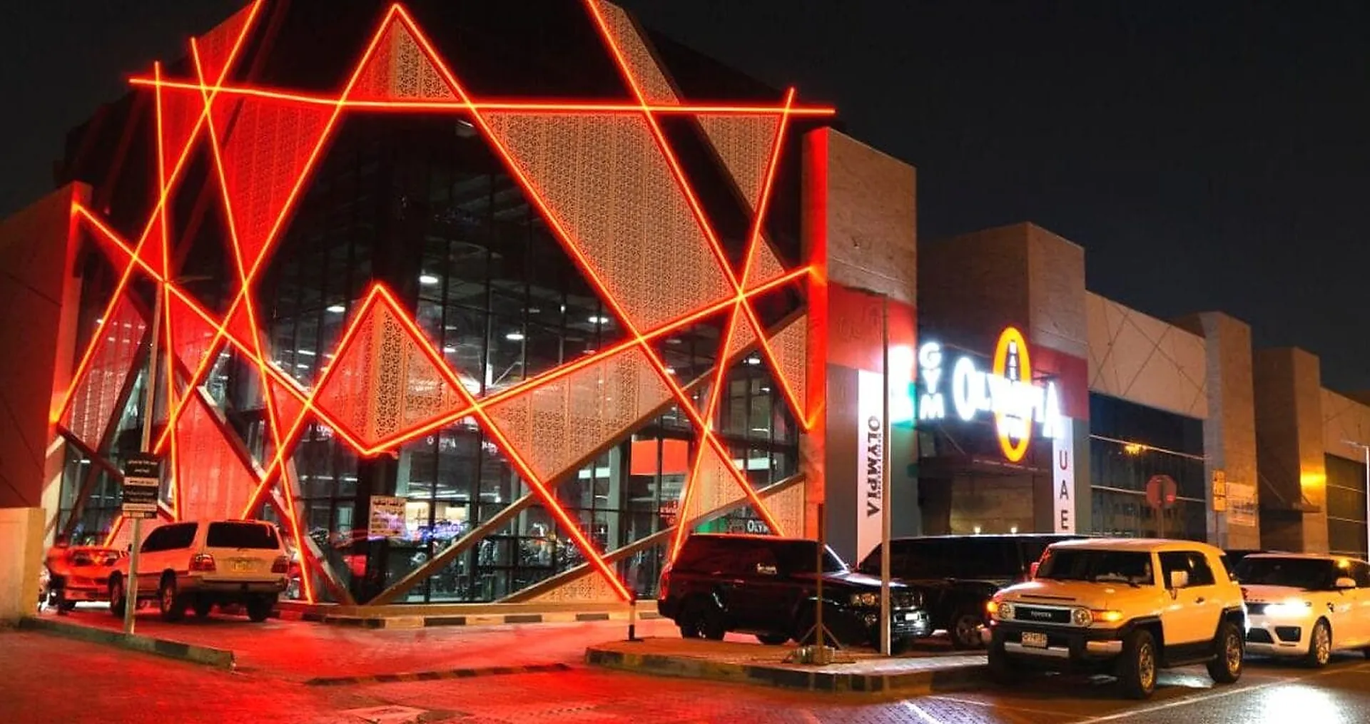 The red-lit geometric screen on the front of Olympia Gym in Sharjah at night