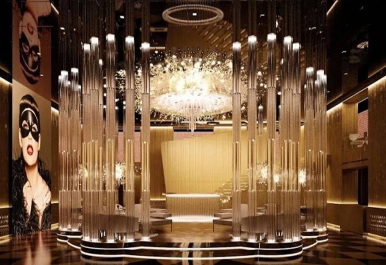 The lobby lounge at Paramount Tower, enclosed by a ring of tall illuminated glass rods with a crystal chandelier behind and a cinema mural on the wall