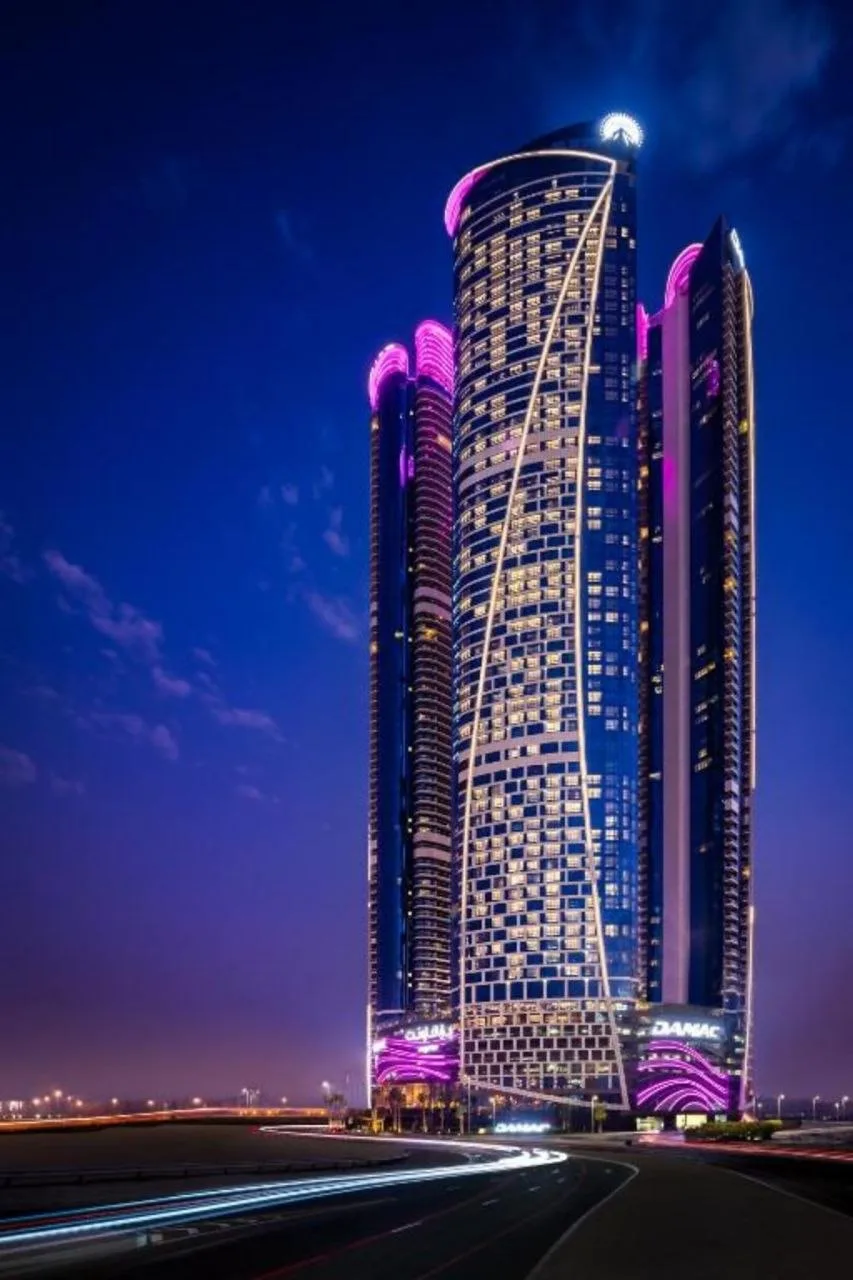The DAMAC Towers by Paramount complex at night, the balcony bands and crown lit in magenta against a deep blue sky