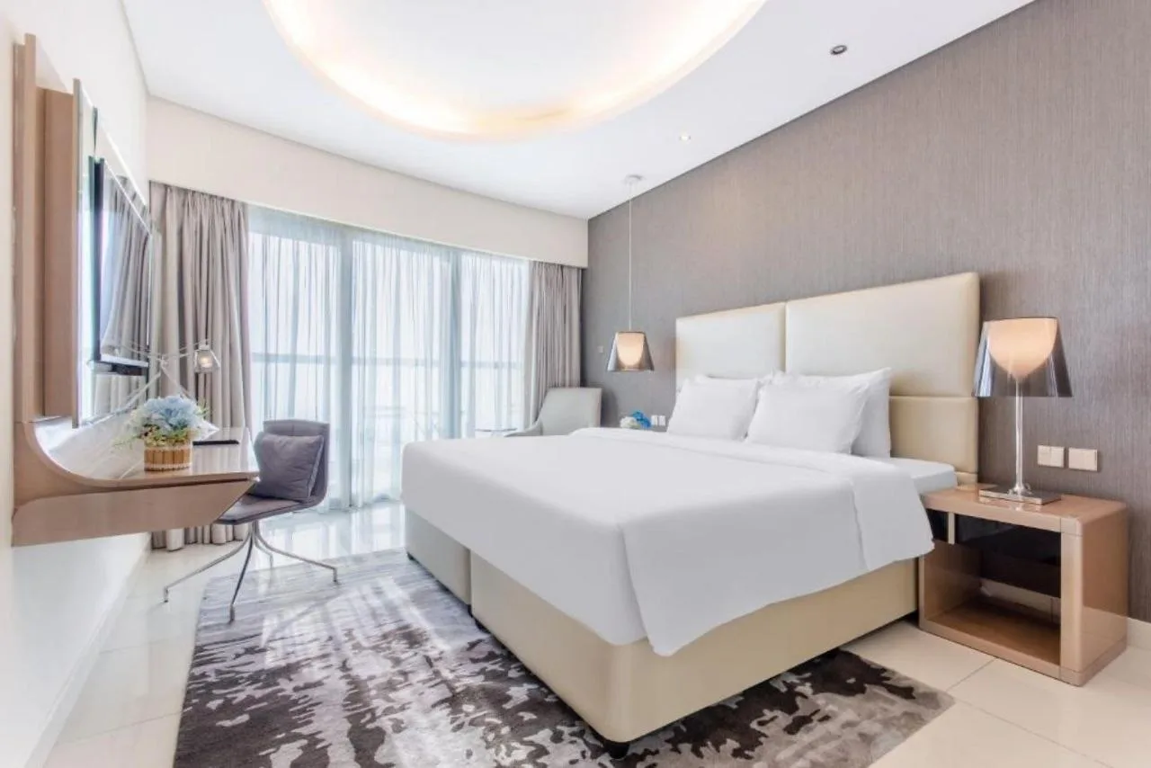 A hotel guest bedroom at Paramount Tower with a circular ceiling cove, two bedside pendants and a lit work desk