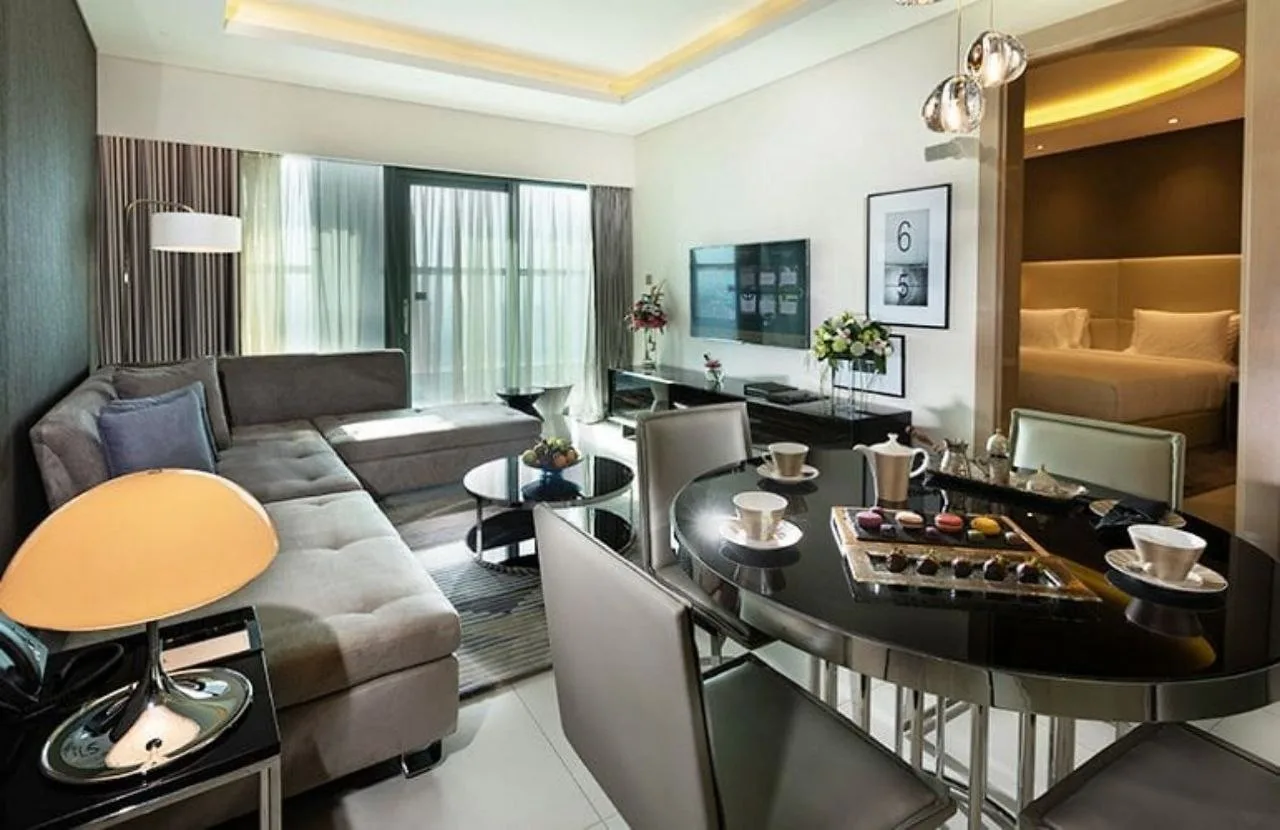 A suite at Paramount Tower where the bedroom opens off the living room, with cove lighting in both and a pendant over the dining table
