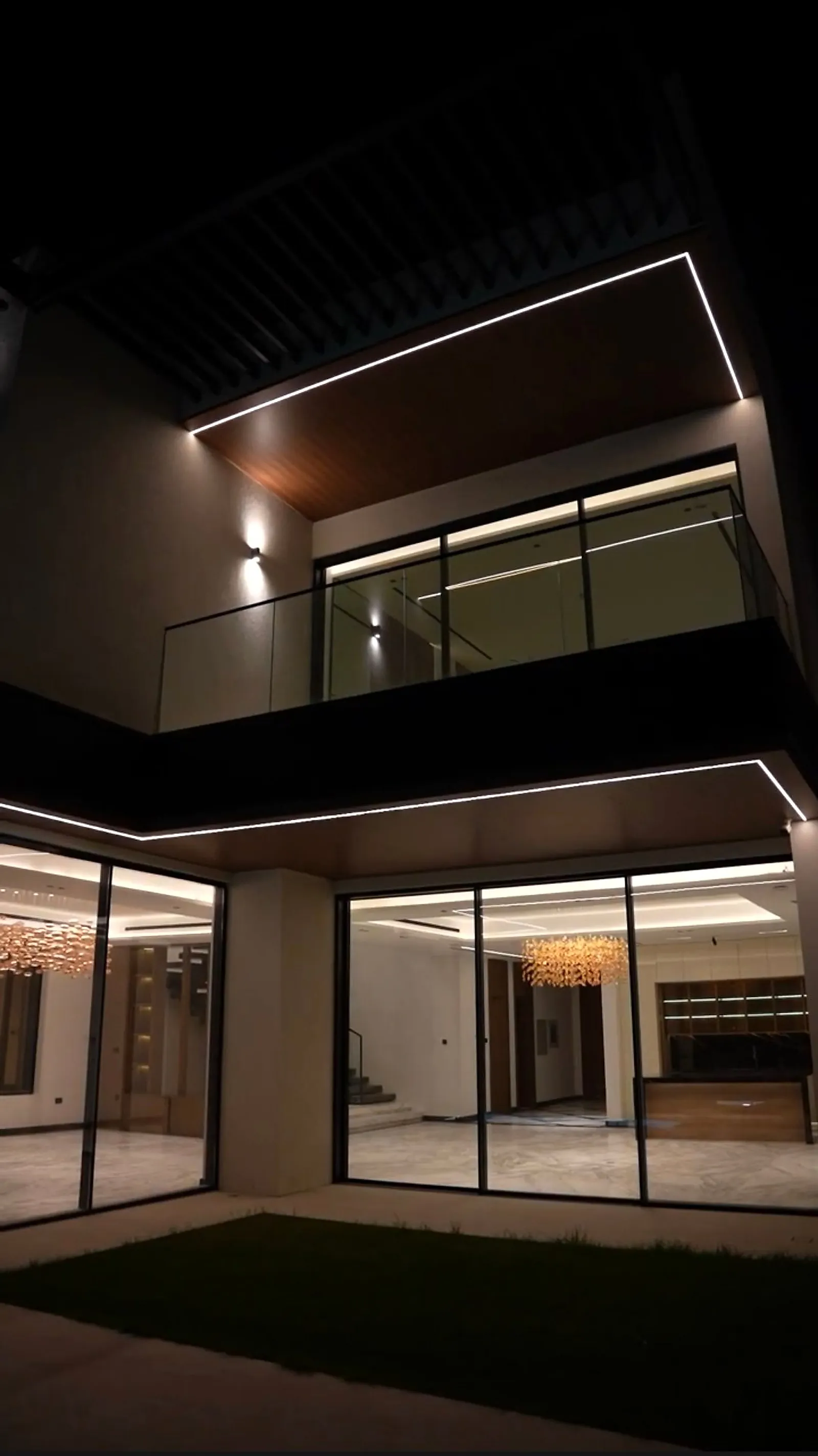 The linear run turning the corner of the villa courtyard, with up-and-down wall fittings below and chandeliers visible through the glazing