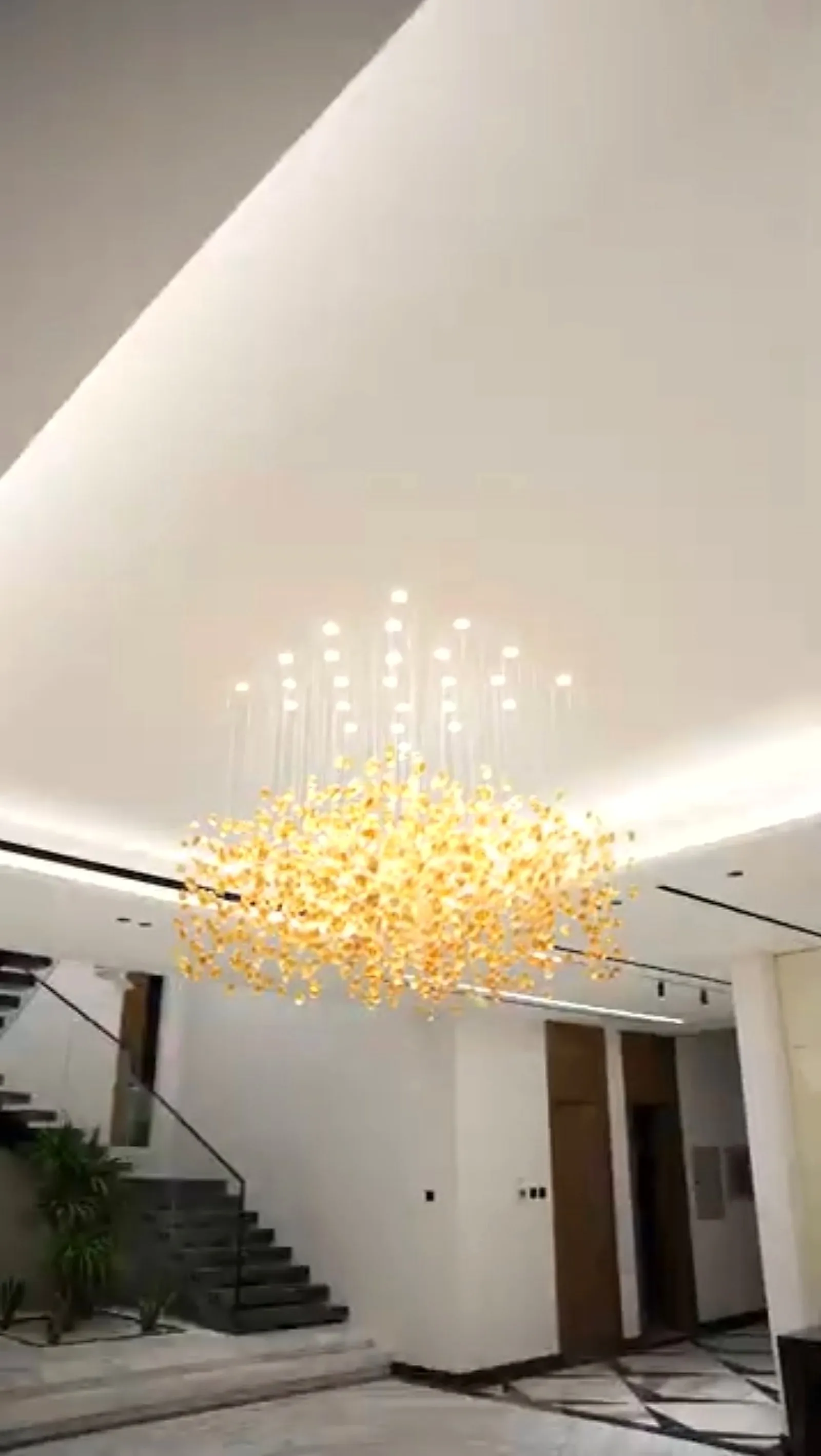 A gold stem chandelier hanging in the double-height hall of a private UAE villa, seen against a cove-lit ceiling