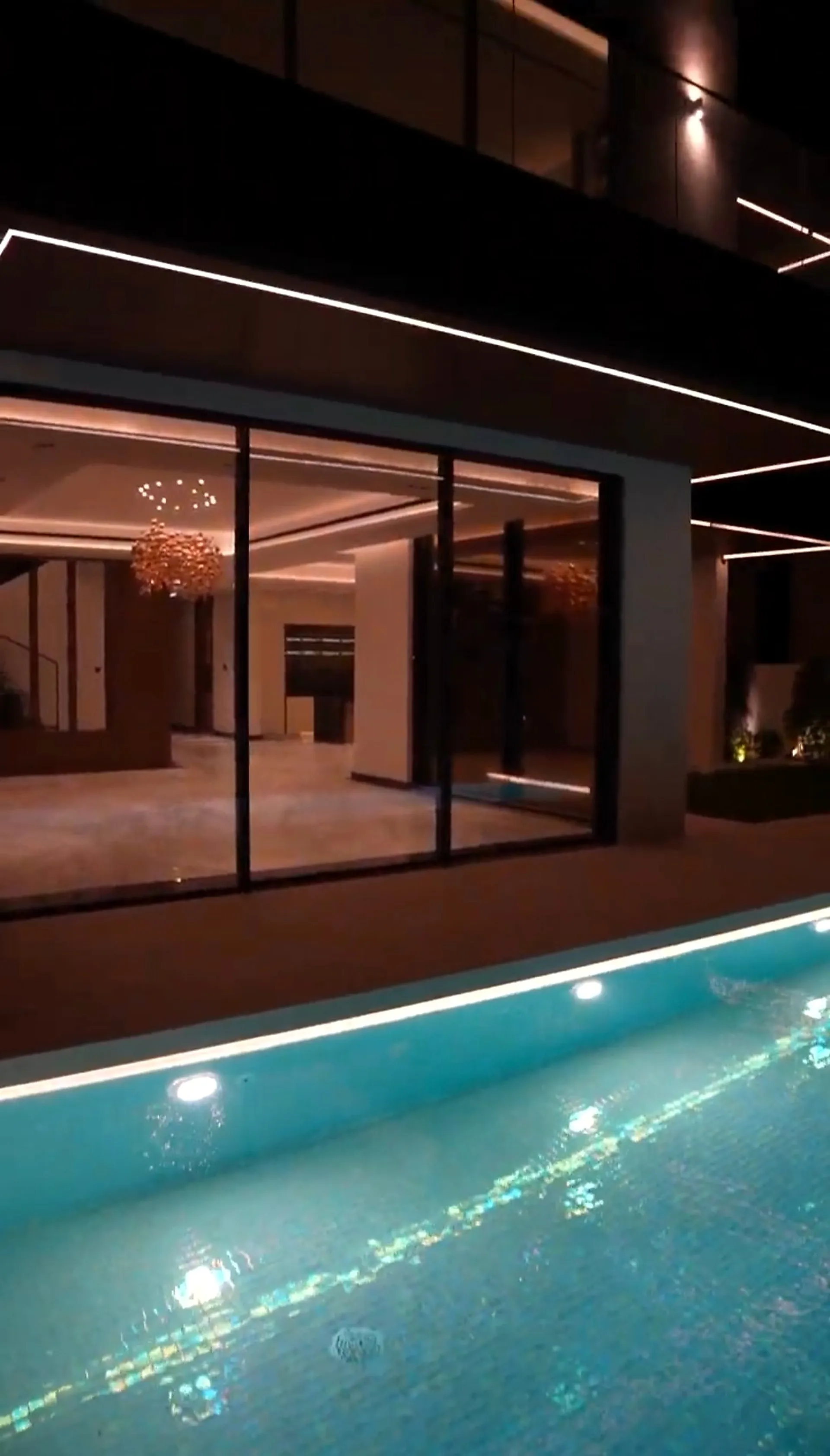 The poolside elevation of a private UAE villa at night, a continuous linear run tracing the soffit above and the pool coping below
