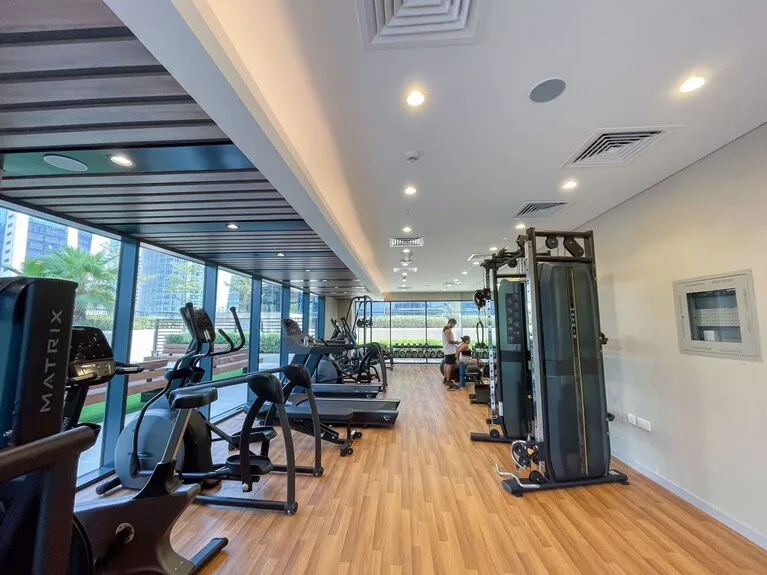 The gym floor at Zada Tower seen from the other end, with treadmills along the glazing and the city beyond