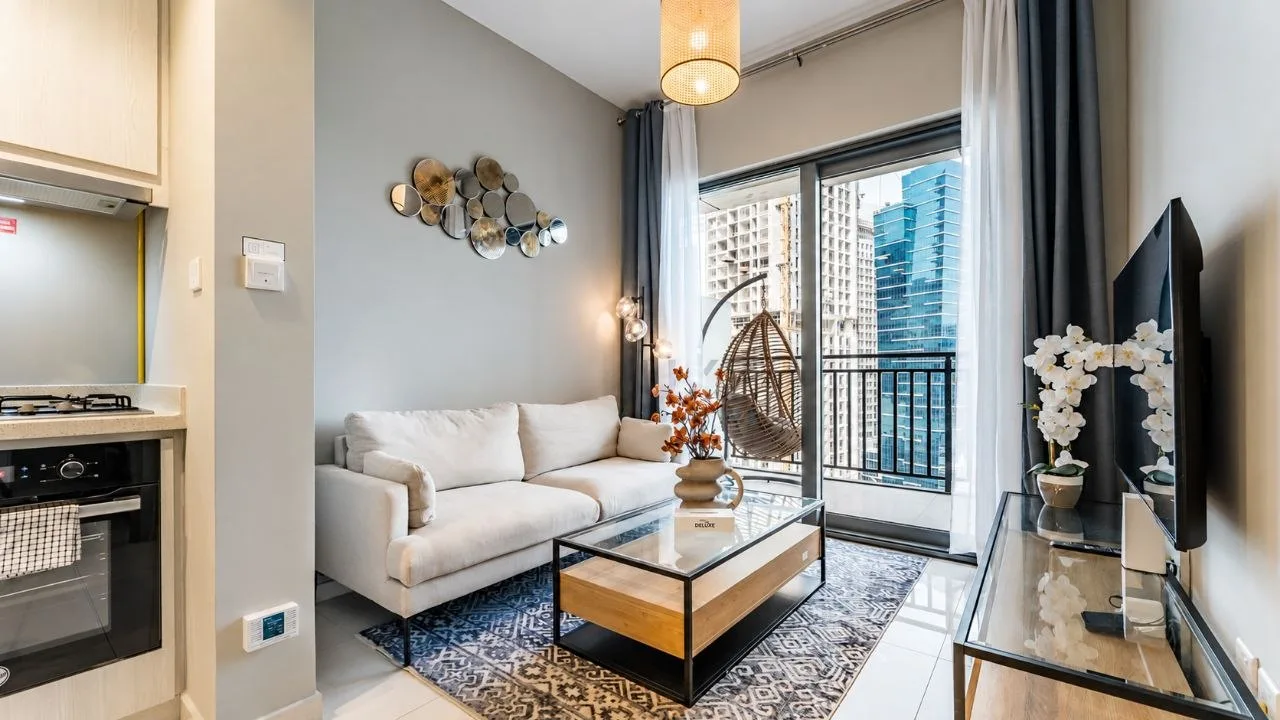 A one-bedroom apartment at Zada Tower with a single drum pendant over the seating, a balcony beyond the glazing and a kitchen at the left